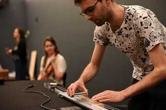 A musician holds a steel tube against the strings of a guitar-like instrument