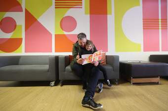 A photograph of a small child and parent looking at a sketchbook in the family space at Tate Liverpool